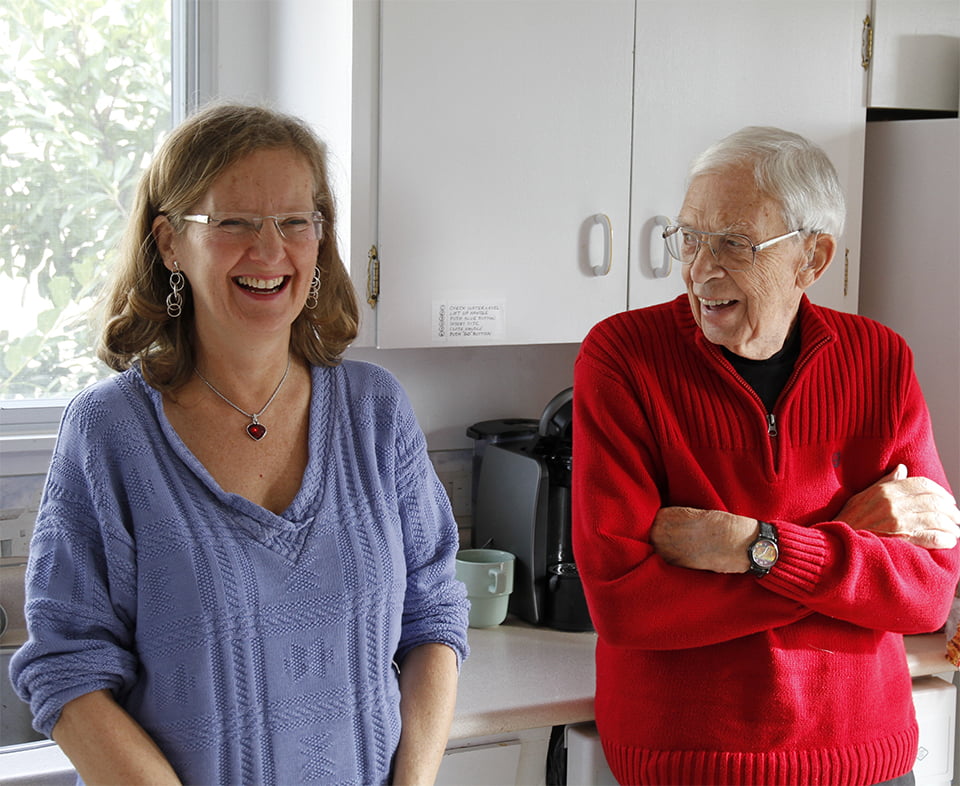 Thelma and ted standing together laughing in the kitchen